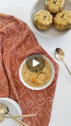 a bowl of soup with spoons next to it on a red towel and two small silver pumpkins