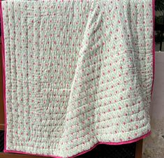 a pink and white quilt on a wooden bench