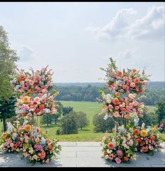 two tall floral arrangements on display in front of a large field with trees and grass