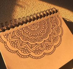 a spiral notebook with an intricate design on the cover, sitting next to a pen