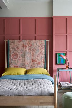 a bedroom with pink walls and a bed in the foreground is a painting on the wall