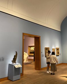 two people looking at some art on display in a room with blue walls and wooden floors