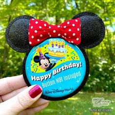 a person holding up a mickey mouse birthday button with a red bow on it's head