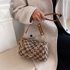 a woman sitting on a bench holding a brown and white checkered purse with gold hardwares