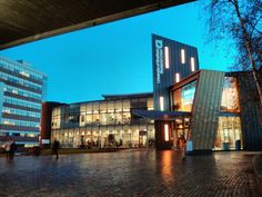 people are walking around in front of an office building at dusk with the lights on