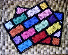 two crocheted coasters sitting on top of a wicker tablecloth covered in multicolored squares