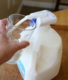 a hand is holding a glass with some liquid in it and a plastic jug next to it