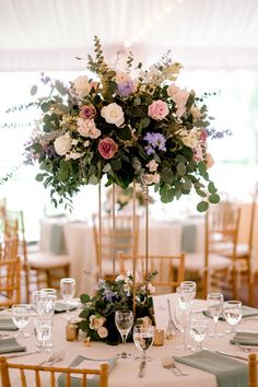 a tall vase filled with lots of flowers on top of a white table cloth covered table