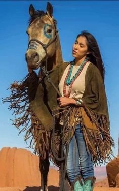 a woman standing next to a horse in the desert