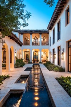 a large white house with a water feature in the front yard and patio area at night