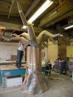 a man standing on top of a piece of cardboard next to a large wooden sculpture