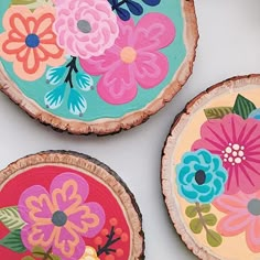 three painted wood slices with flowers on them sitting on a white table top next to each other