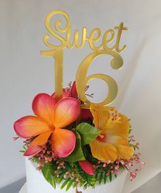 a white cake topped with flowers and a gold sweet sixteen sign on it's top