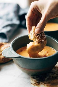 a person dipping something into a bowl of soup with bread on the table in the background