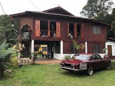 an old car is parked in front of a large wooden house with balconies