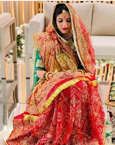 a woman sitting on top of a white chair wearing a red and gold wedding dress