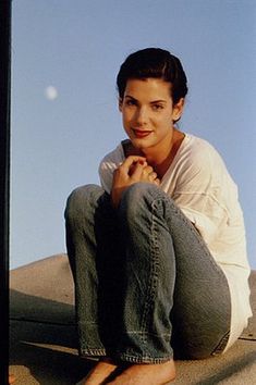 a woman sitting on top of a cement wall next to a window with her hand under her chin