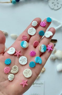 a hand holding several different colored seashells and shells