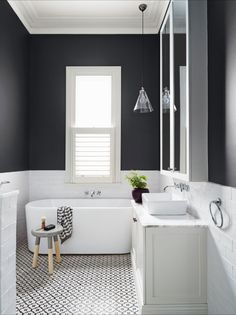 a white bath tub sitting under a bathroom window next to a sink and a mirror