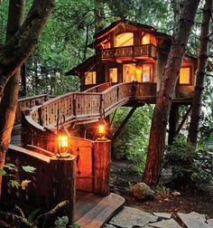 a tree house in the woods with stairs leading up to it's roof and lights on