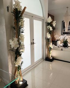 a living room filled with furniture and flowers on top of a white tiled floor next to a doorway