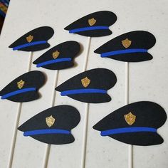 six police hats are lined up on a white table with blue and gold trimmings