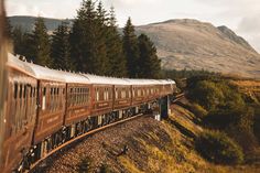 the train is traveling down the tracks in the mountainside area with trees on both sides