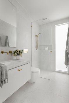 a white bathroom with gold accents and marble counter tops, along with a large window