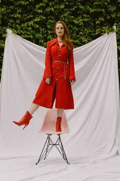 a woman standing on top of a chair in front of a white backdrop wearing red boots