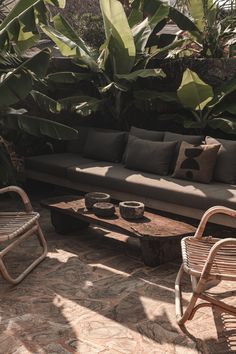 a couch and two chairs sitting on top of a stone floor next to some plants