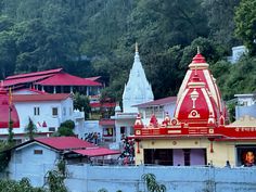 a red and white temple in the middle of some buildings with trees behind it on a hill side