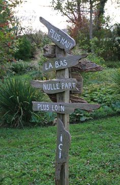 a wooden pole with several signs on it in the middle of a grassy area next to bushes and trees