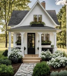 a small white house with black shutters and flowers on the front door is shown