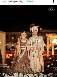 two people standing next to each other in front of white flowers and lights at night