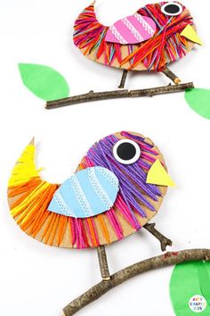 two colorful birds sitting on top of branches with green leaves and one bird is made out of construction paper