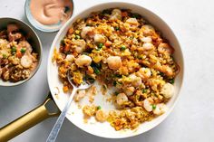 two bowls filled with food on top of a white table next to gold spoons