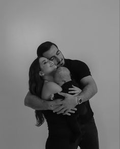 a man and woman hug each other while holding a baby in their arms, black and white photo