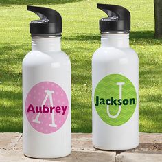 two personalized water bottles sitting next to each other on a stone slab in the grass