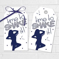 two tags with the words time to shake and a woman in silhouette on them, hanging against a white brick wall