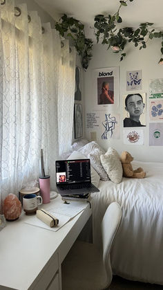 a laptop computer sitting on top of a white desk in front of a window covered with plants