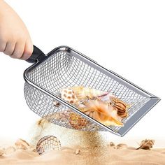 a person scooping sea shells out of the sand with a metal mesh strainer