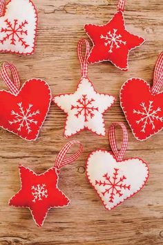 four red and white heart shaped ornaments on a wooden surface with snowflakes hanging from them