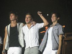 three young men standing next to each other on stage with their arms in the air