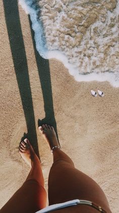 the shadow of a person's feet on the sand next to the water and beach