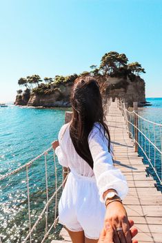 a woman walking across a bridge next to the ocean