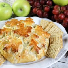 a white plate topped with crackers and an apple next to some grapes on a table