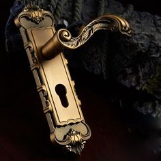 an ornate brass door handle on a wooden table next to a mossy stone wall