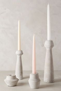 three white candles sitting next to each other on top of a cement table with one candle in the middle