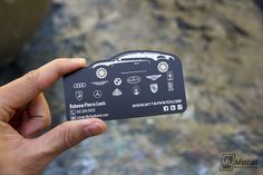 a hand holding up a black business card with different car logos on the front and back