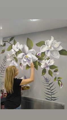 a woman is painting flowers on the wall